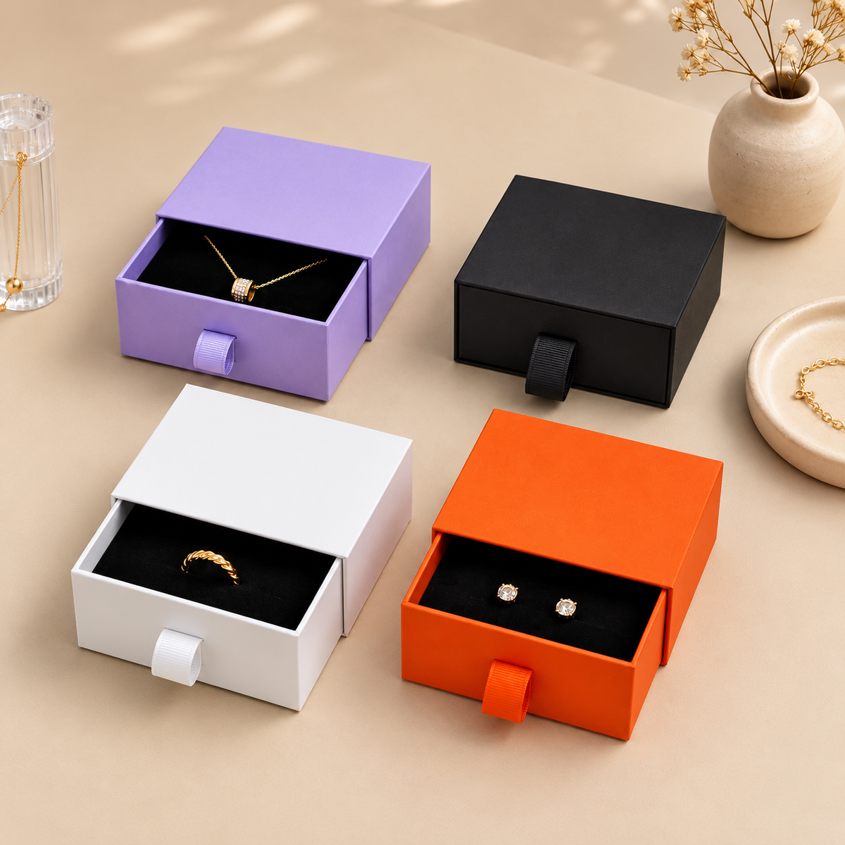 Open paper drawer jewelry boxes with black inserts in purple, white and orange, beside a closed black box
